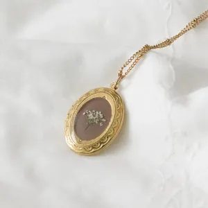 Nahaufnahme einer Vintage-Medaillon-Halskette aus 14k Gold mit weißen Trockenblumen