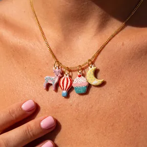 Detalle de collar dorado con dijes de esmalte de colores: ciervo, globo, cupcake y luna.