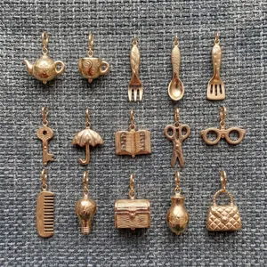 Collection de 15 breloques miniatures en acier doré sur fond de tissu gris.