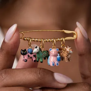 Detalle de primer plano de un broche de imperdible dorado con dijes de animales pintados