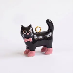 Vista detallada de un colgante de gato negro brillante con lazo rosa y pequeñas botas