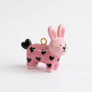 Primer plano de un colgante de conejo rosa con patrones de corazones negros y aro dorado