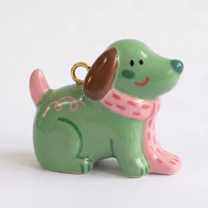 Primer plano de un colgante de perro de cerámica verde con bufanda rosa y aro dorado