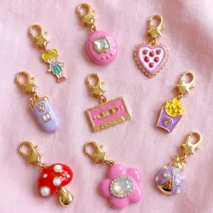 A collection of nine vibrant Y2K style enamel charms with gold lobster clasps on pink fabric