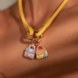 Detailed close-up of two cute enamel bag charms on a vibrant yellow necklace cord
