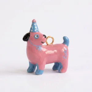 Detalle de un colgante de perro de cerámica rosa con sombrero azul y anillo dorado