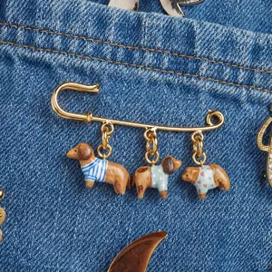 Broche épingle à nourrice dorée avec breloques chien et ours sur une veste en jean