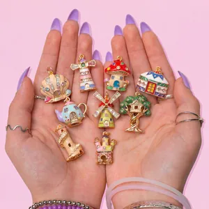 Colorful enamel fairy tale cottage pendants held in hands, showcasing intricate details