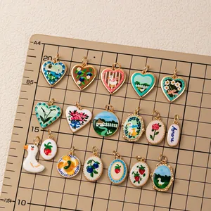 Close-up of pastoral enamel charms with blueberry, duck, and rose motifs on a grid board.