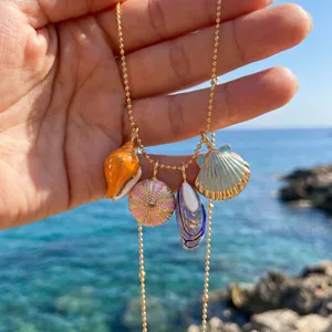 Detailed view of hand-painted shell charms on a gold bead necklace by the ocean.