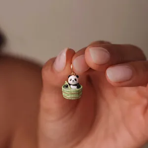 Detailed view of a cute panda bathing in a bamboo tub charm held between fingertips.