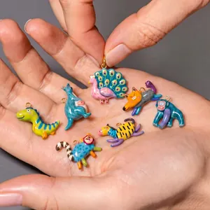 Close-up of vibrant hand-painted enamel animal charms including peacock and dinosaur in hand