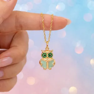 Detailed macro shot of a gold owl pendant necklace featuring green eyes and book design