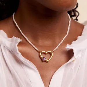 Dettaglio di un ciondolo a cuore in oro con gemma viola su collana di perle.