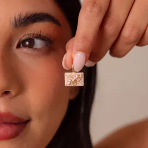 Close-up of pink envelope pendant with cherry blossom detailing held by fingers