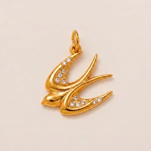 Pendentif hirondelle doré avec cristaux étincelants sur un fond beige texturé élégant