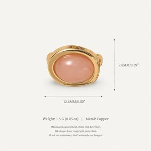 Detailed view of a golden copper oval charm featuring a smooth peach pink stone cabochon