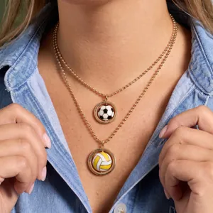 Détail rapproché de colliers dorés superposés avec pendentifs foot et beach volley