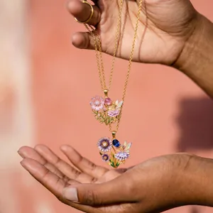 Detailed macro shot of fairy flower enamel necklaces held in hand showing intricate petals.