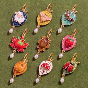 Collection of nine colorful enamel leaf pendants with cute animal and fruit motifs.