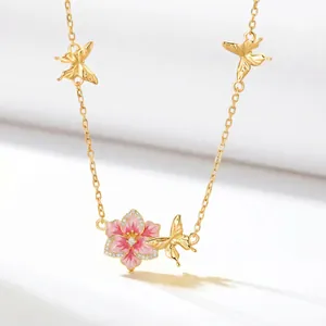 Detailed macro view of golden chain necklace with pink enamel flower and gold butterflies.