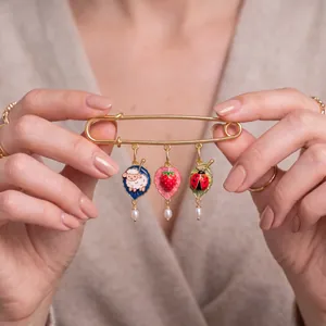 Close-up of enamel leaf charms with sheep, strawberry, and ladybug on a gold pin.