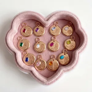 Macro detail of twelve rose gold birth flower pendants with birthstones in heart tray