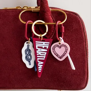Vintage heart and Heartland slogan bag charms attached to a red suede handbag detail.
