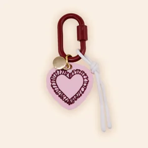Close-up of a pink heart-shaped bag charm with a red metal carabiner and white cord