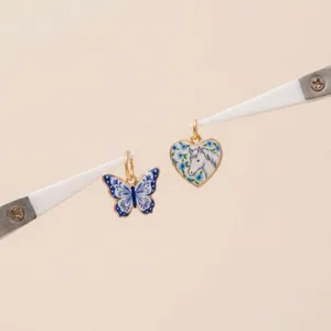 Detail shot of fairy tale style butterfly and heart horse pendants held by tweezers.