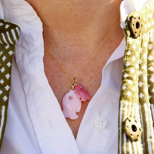 Close-up of pink and coral fish-shaped pendants on a delicate gold chain necklace worn by model