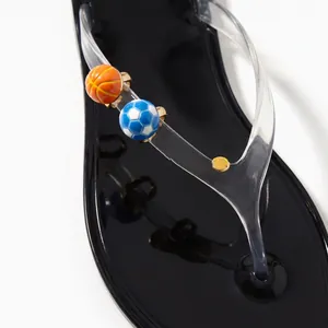 Detailed view of mini basketball and soccer enamel shoe charms on a clear flip-flop strap