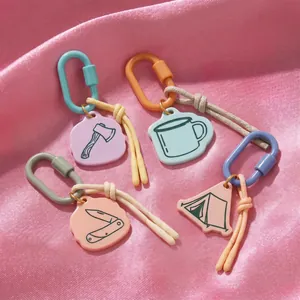 Détail de quatre breloques de camping en acrylique coloré avec mousquetons sur tissu rose