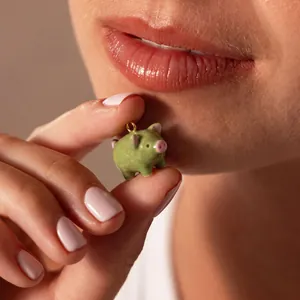 Vue macro d'un joli pendentif cochon en émail vert tenu par des doigts près du visage