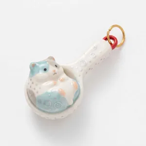 Dettaglio di un ciondolo a cucchiaio in ceramica con criceto e anello dorato per gioielli.