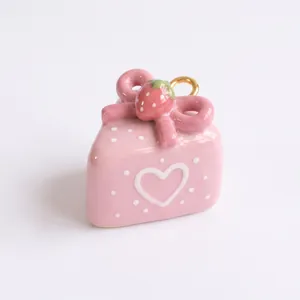 Vue détaillée d'un pendentif gâteau rose à motif cœur avec fraise et nœud décoratif.