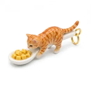 Dettaglio di un simpatico ciondolo a forma di gatto soriano arancione su un cucchiaio bianco