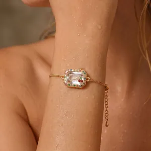 Close-up of a gold rainbow crystal frame bracelet with LOVE charm and water droplets.