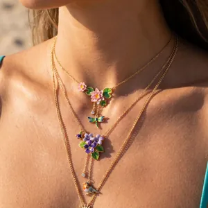 Primo piano di una collana smaltata vintage con ciondoli floreali, una libellula e un uccello.