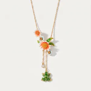 Primo piano di collana vintage dorata con fiori smaltati e ciondolo a rana verde carino