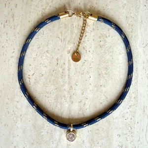 Close-up of blue woven cord choker with gold thread and round sparkling zircon pendant.