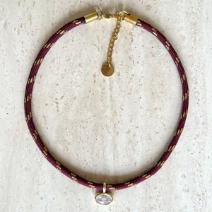 Close-up detail of a burgundy braided choker with gold silk thread and a zircon pendant