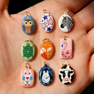 Collection of colorful hand-painted enamel animal pendants displayed on a human palm.