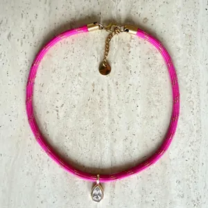 Macro view of a pink braided choker with a teardrop zircon pendant and gold hardware