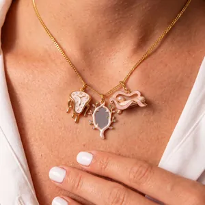 Primer plano de un collar dorado con dijes de reloj derretido y sofá surrealista.