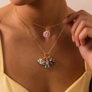 Close-up detail of layered gold necklaces featuring enamel flower charms and pink rose