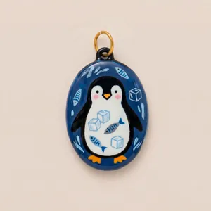 Close-up of hand-painted enamel penguin pendant with fish and ice cube motifs