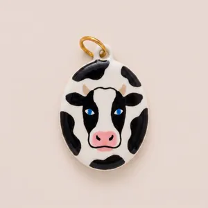 Close-up of hand-painted enamel cow pendant with glossy finish and vibrant blue eyes.
