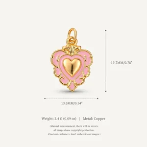 Dettaglio di un ciondolo a cuore rosa in rame con volute dorate ornate e dimensioni