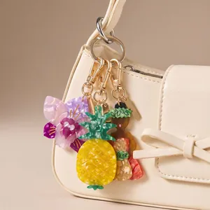 Primer plano de colgantes acrílicos de piña y hula girl decorando un bolso blanco
